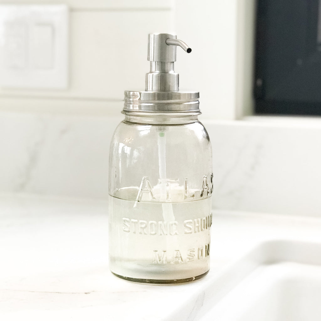 Stainless soap pump on vintage Atlas Strong Shoulder Mason Regular Mouth Quart Jar on white quartz countertop next to white farmhouse sink